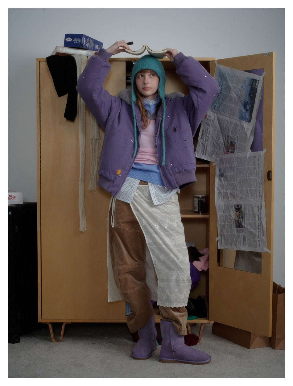 Model in a purple plush-collar jacket, arms raised while holding an open book above her head.