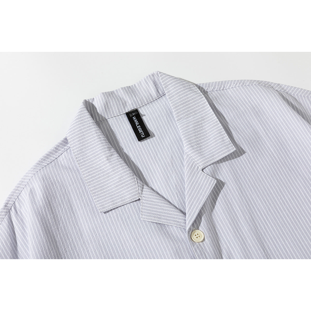 Close-up of a light gray striped shirt showing its notched collar, cream button, and black neck label.