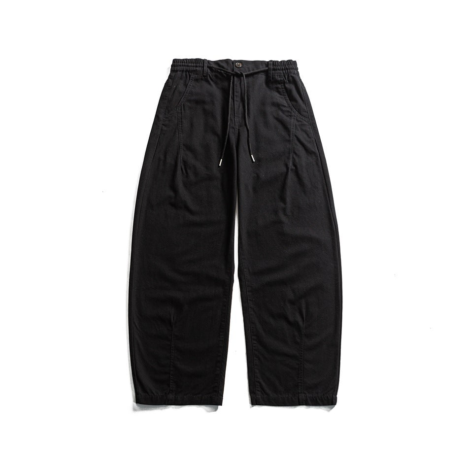 Front view of black wide-leg trousers with an elasticated waist, drawstring, button closure, and angled pockets.