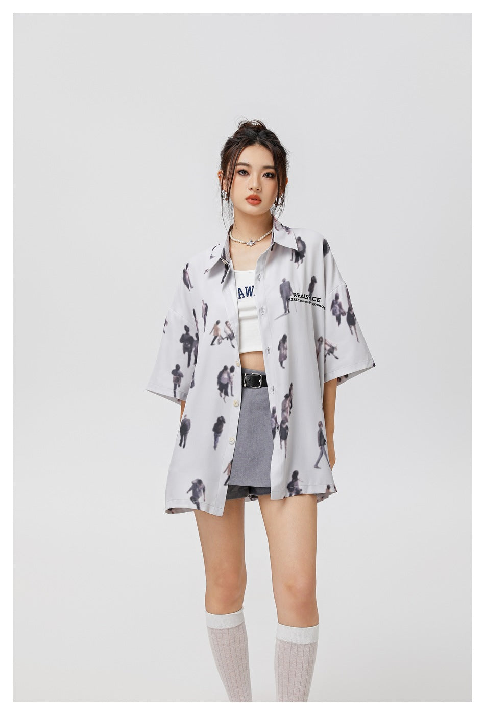 Model wearing an oversized pale gray short-sleeve button-up shirt with a scattered miniature-people print.
