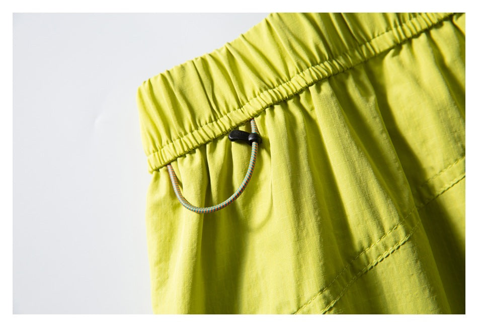 Close-up of lime-yellow shorts' elastic waistband with a looped multicolored drawcord and black toggle.
