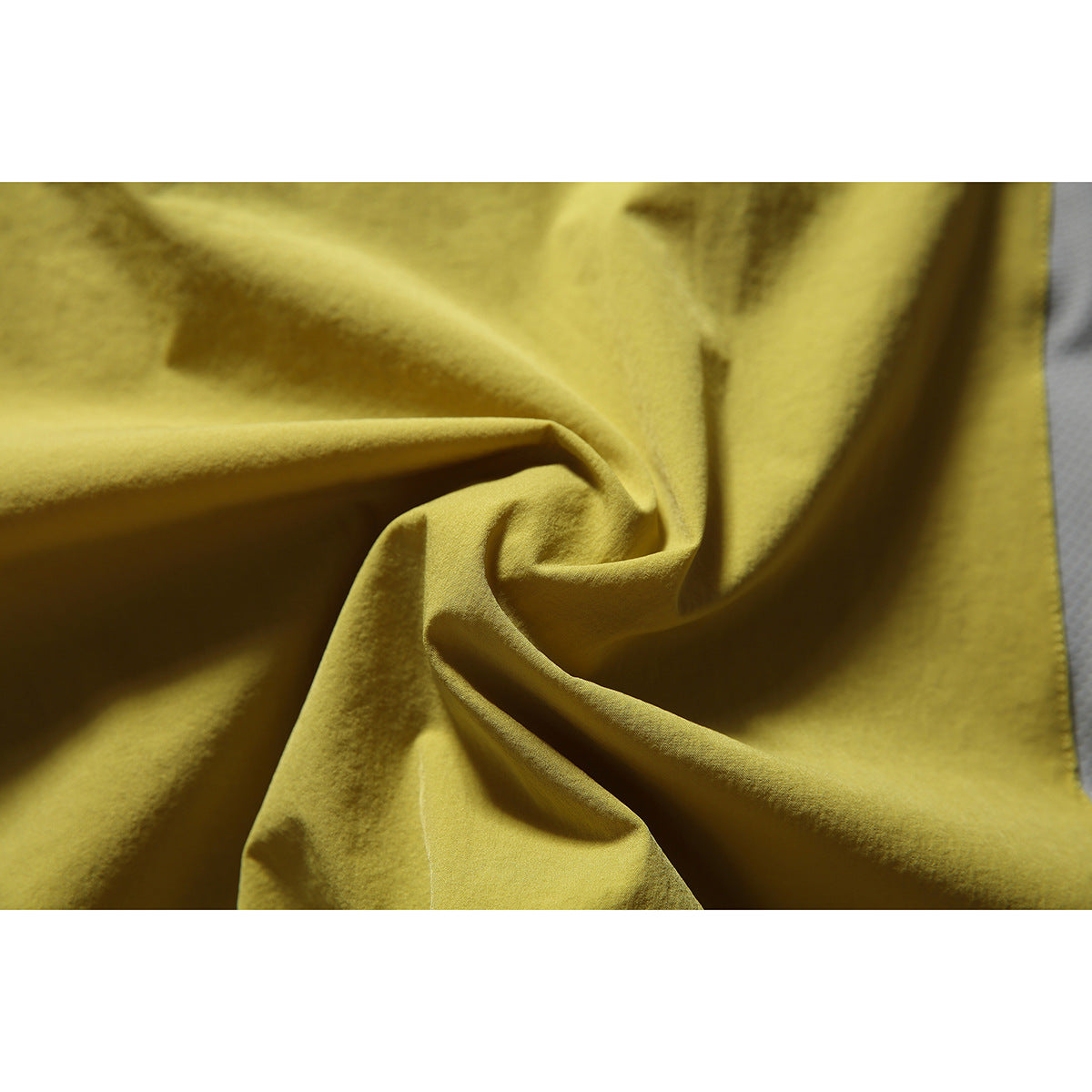 Close-up of mustard yellow-green vest fabric gathered into folds, with a narrow gray panel at the edge.