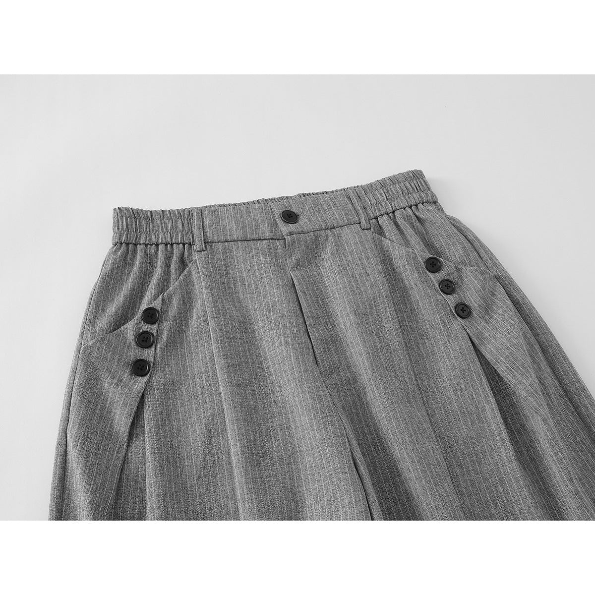 Close-up of gray pinstripe wide-leg trousers showing the elastic waistband, front button, pleats, and side button tabs.