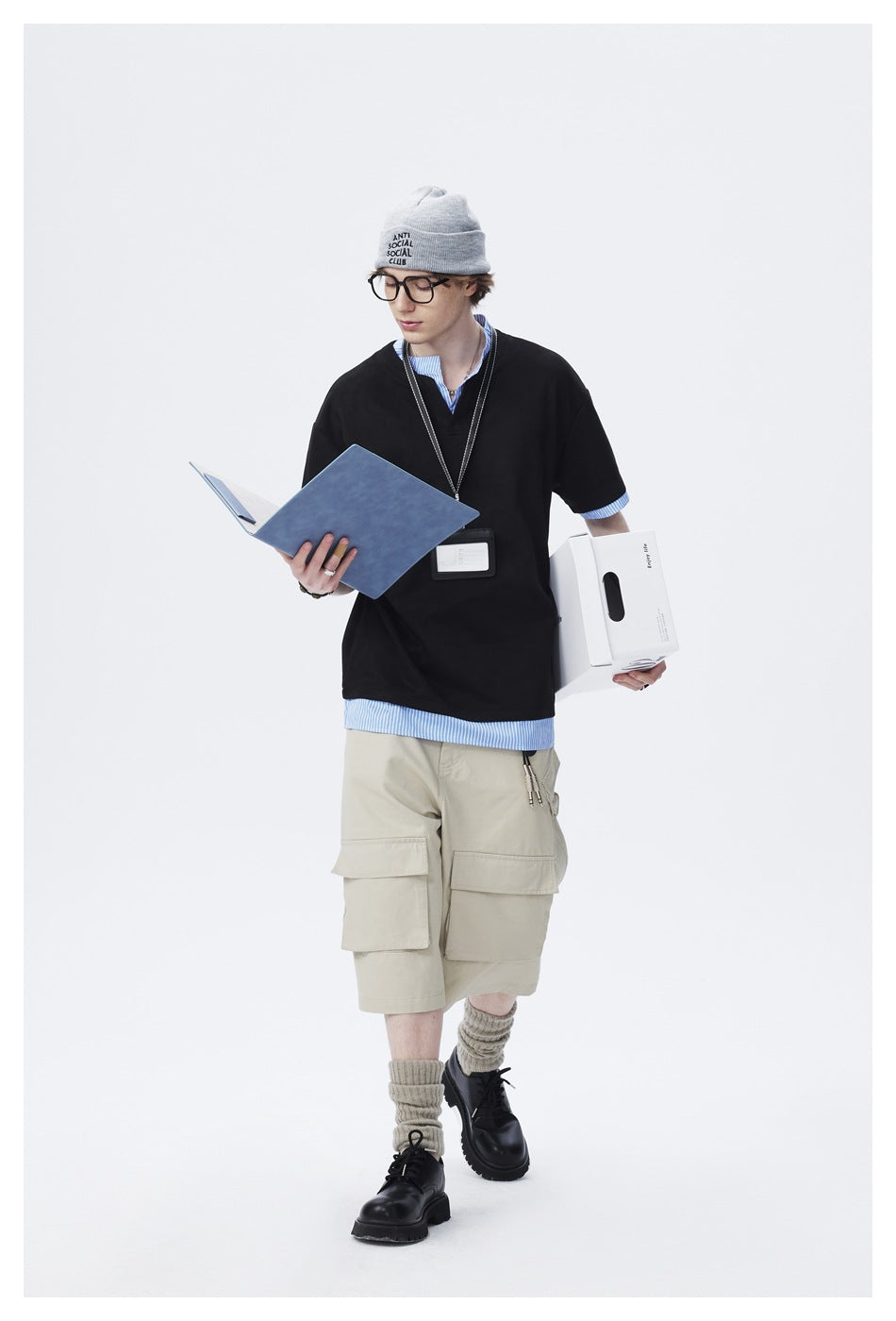 Full-length model wearing an oversized black top with blue striped trim and beige cargo shorts.