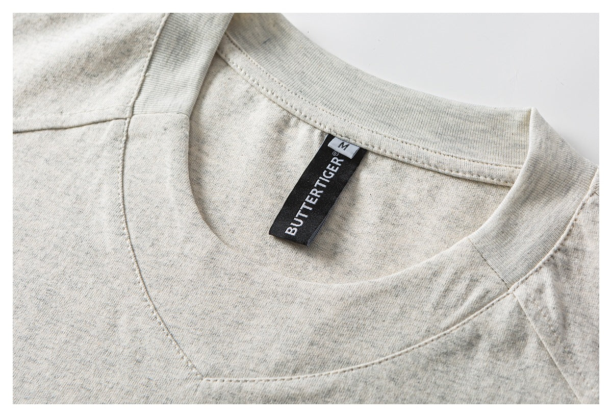 Close-up of a ribbed crew neckline and black “BUTTERTIGER” size M label on a light gray heathered top.