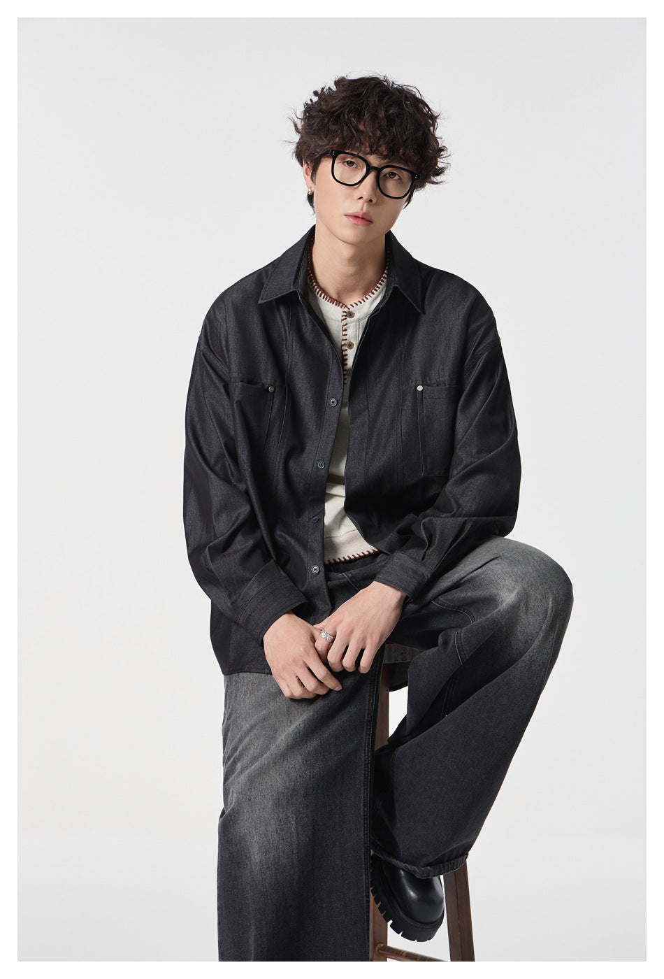 Closer seated view of a model wearing a dark charcoal button-up shirt with two chest pockets over a cream top.