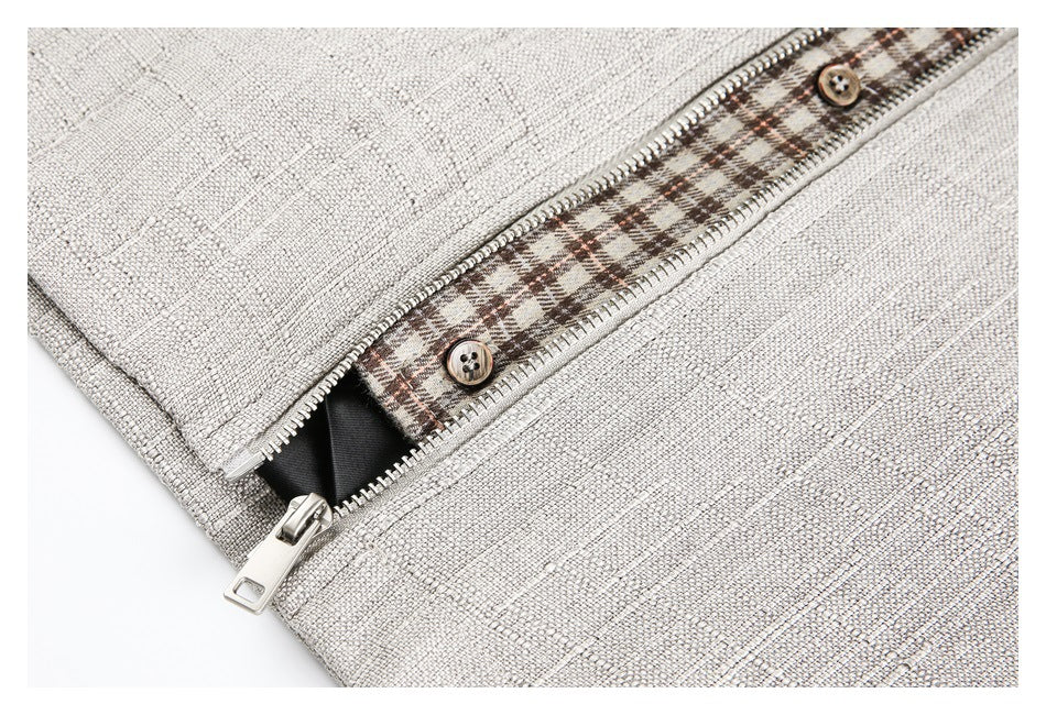 Close-up of a light beige textured garment with a metal zipper, brown buttons, and brown plaid trim.