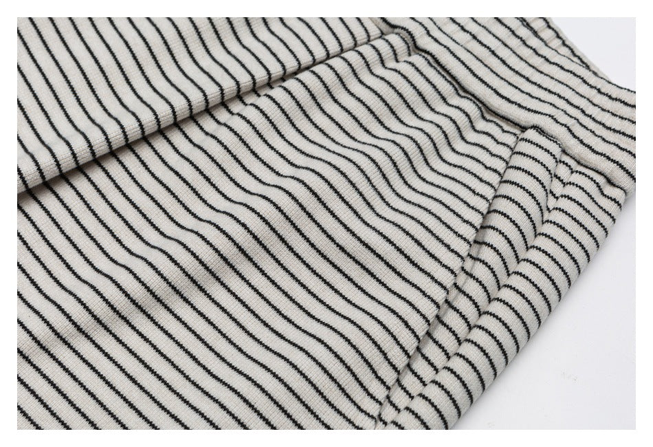 Close-up of off-white ribbed knit fabric with thin black stripes, folded in soft diagonal layers.