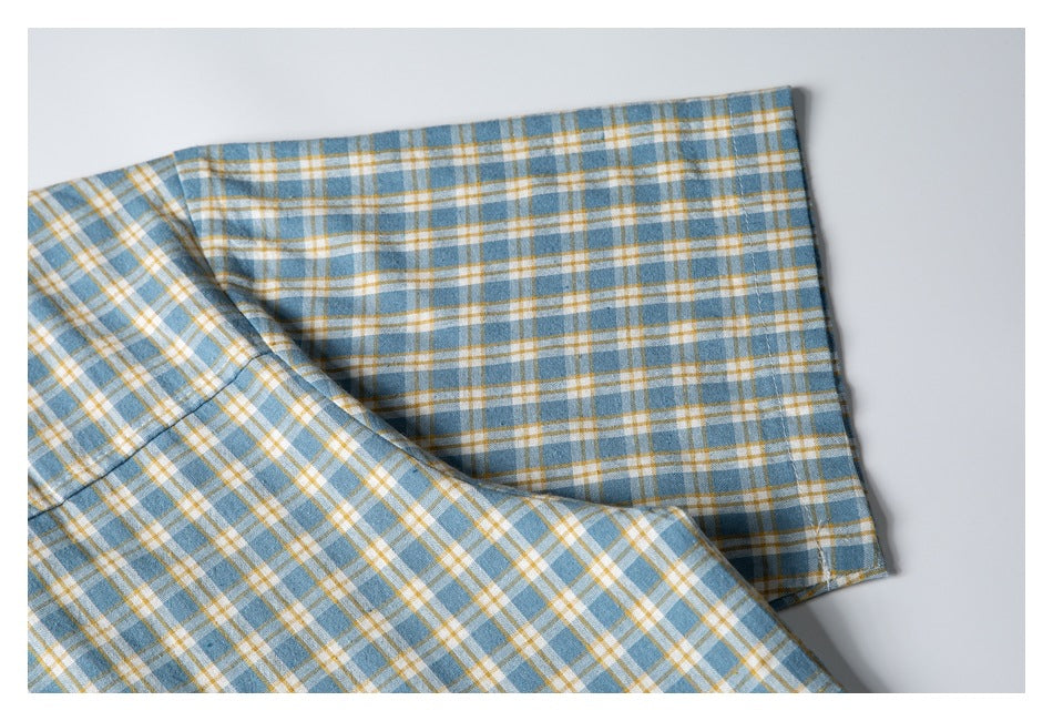Close-up of a plaid shirt sleeve cuff in blue, white, and mustard, with the cuff folded back.