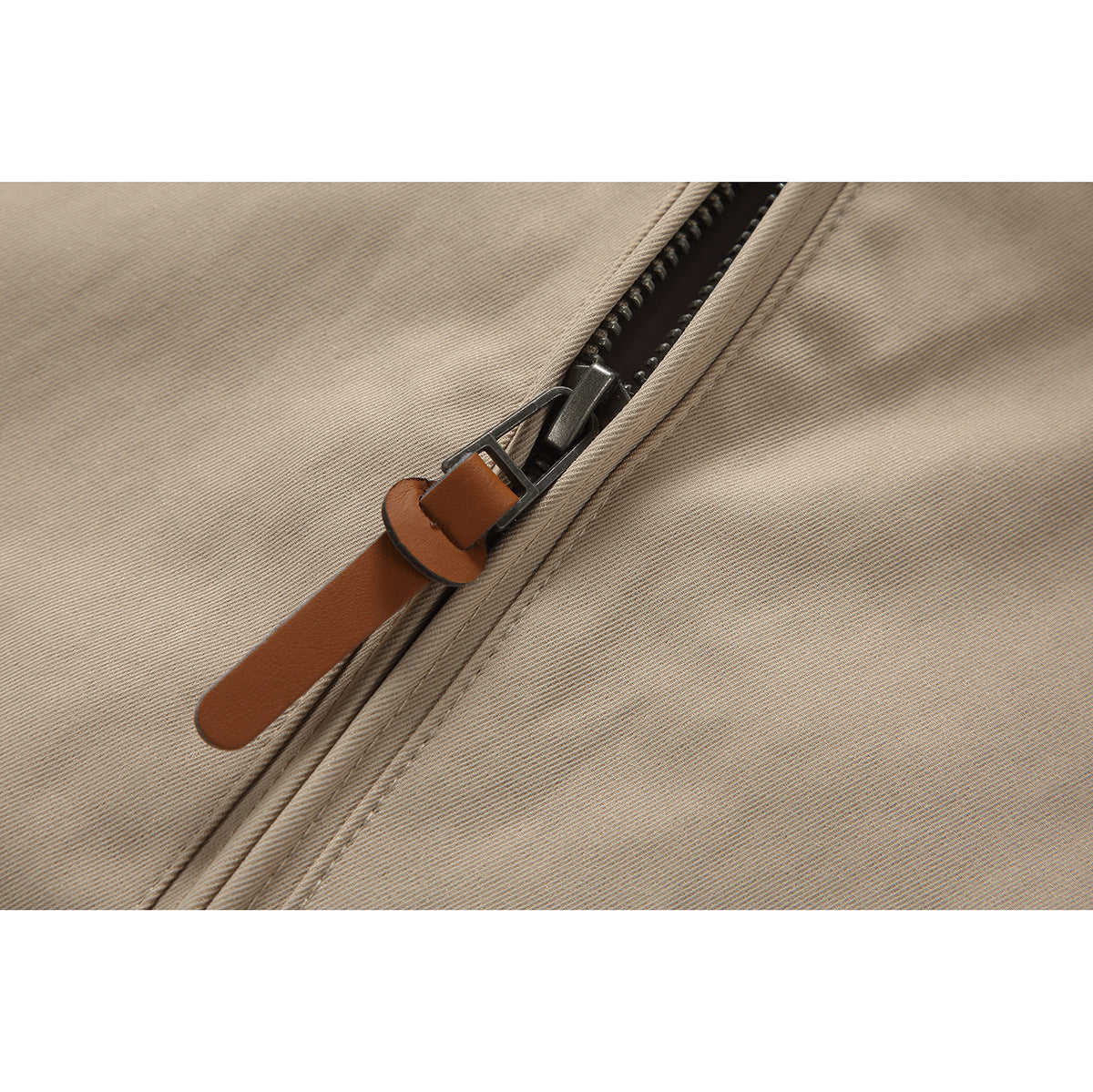 Close-up of a beige jacket's dark zipper and long brown pull tab.