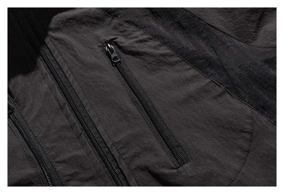 Close-up of a dark charcoal garment with black zippers, a zip pocket and textured paneling.