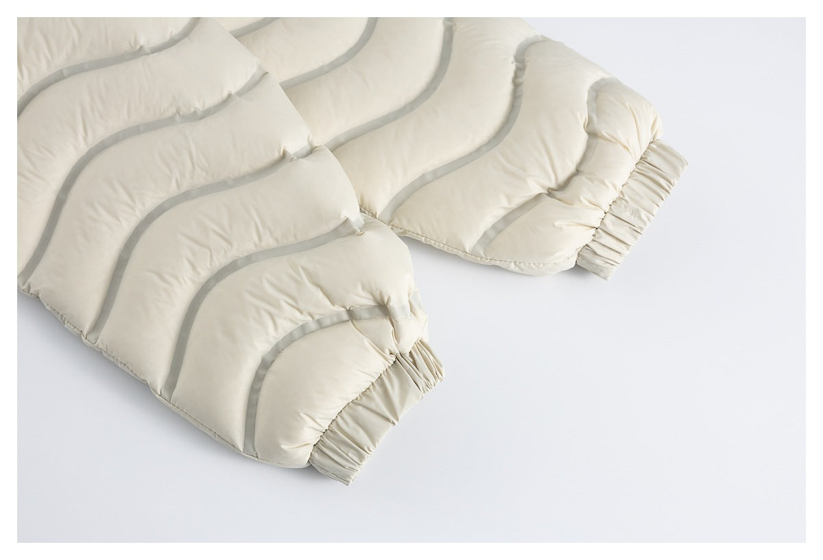 Close-up of an ivory quilted puffer jacket with curved gray piping and gathered elastic cuffs.