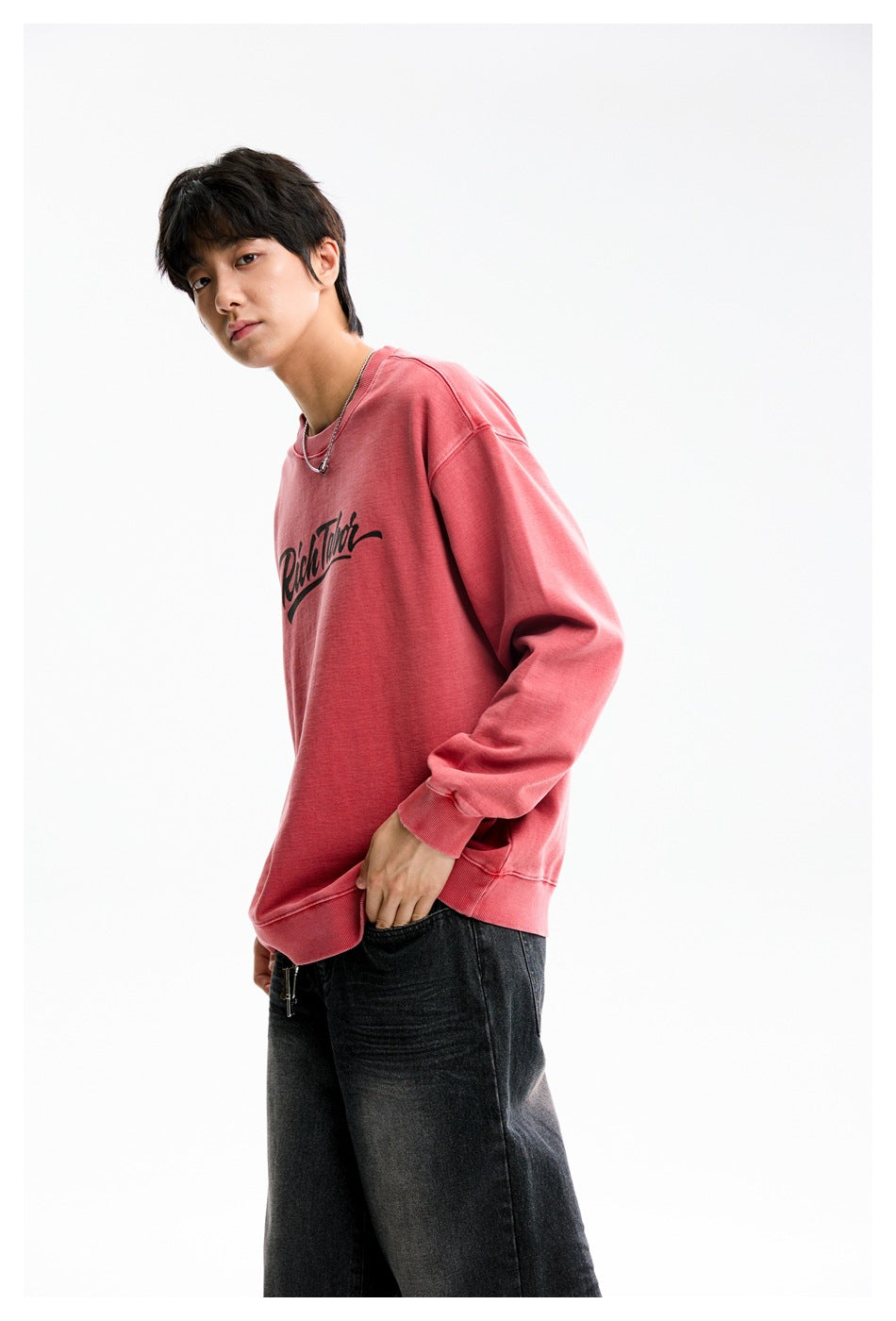 Side-angle view of a model wearing a dusty-rose crewneck sweatshirt with black script print and black jeans.