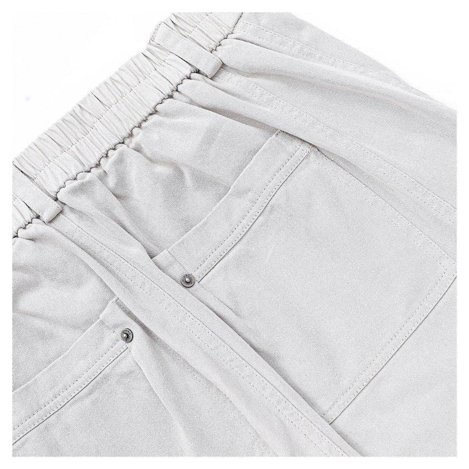 Close-up of light gray pants showing an elastic waistband and large stitched front pockets with snap buttons.