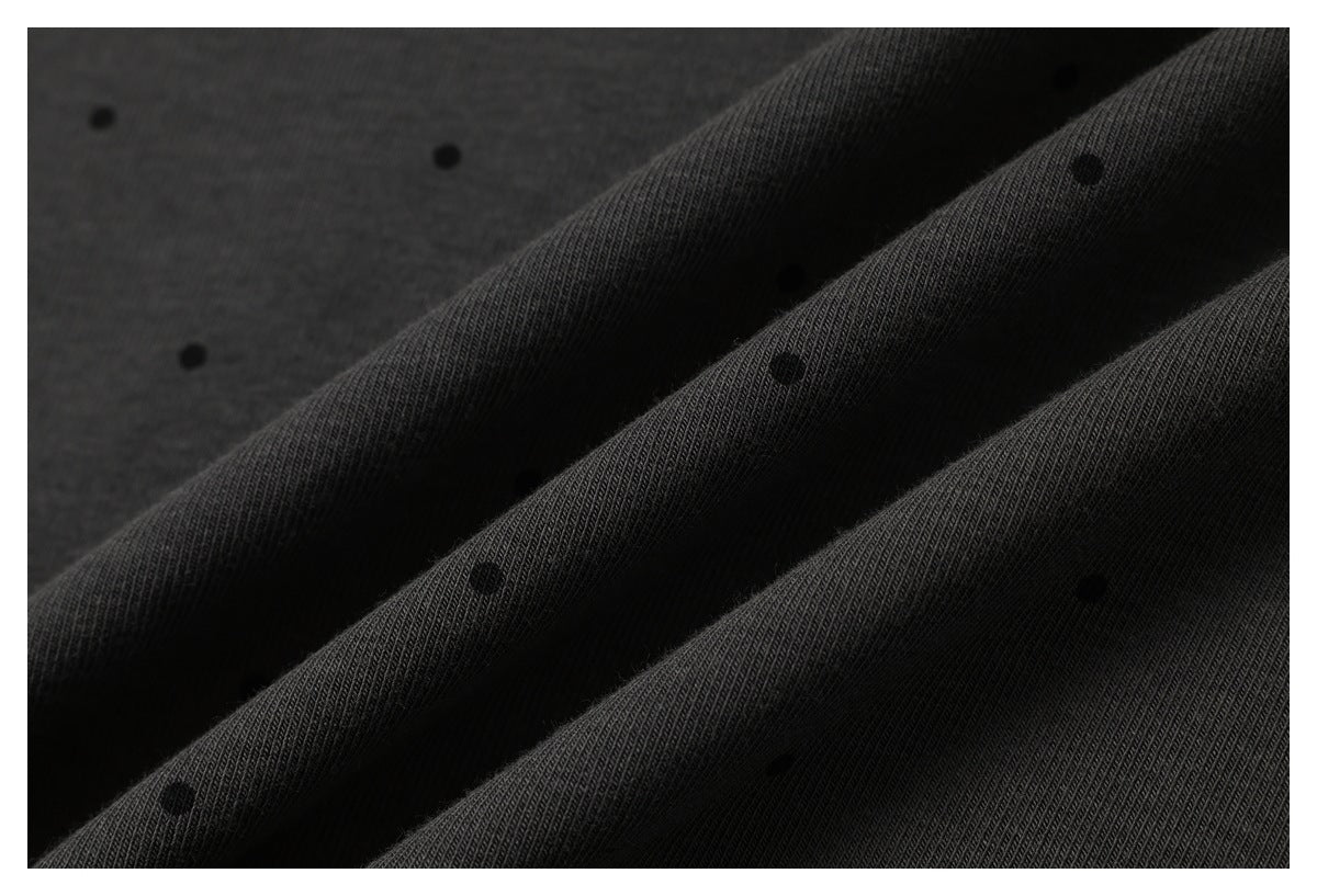 Macro view of charcoal T-shirt fabric folded into ridges, showing its fine knit texture and scattered black dots.
