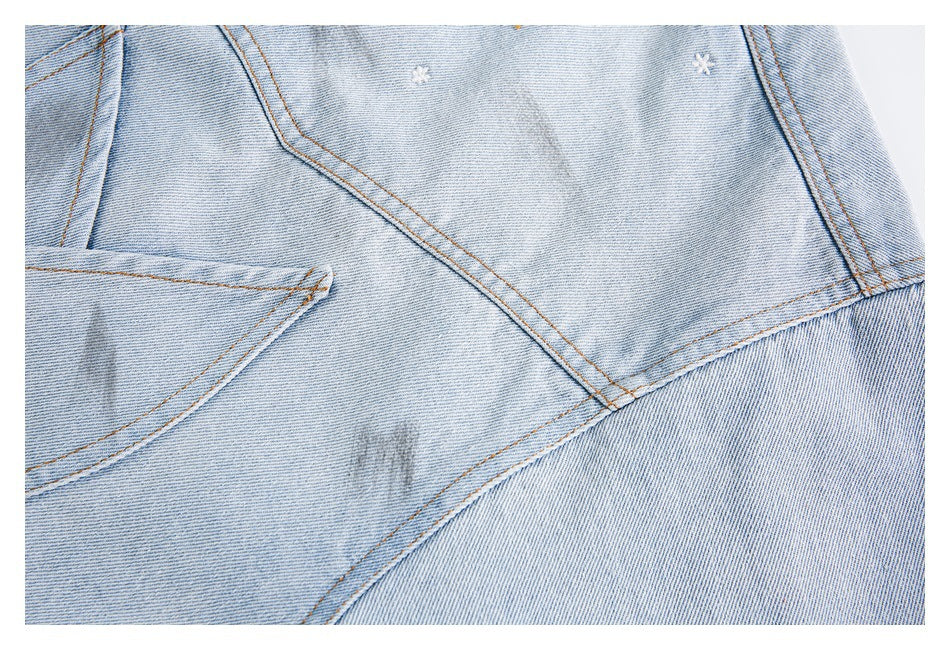 Close-up of light-wash denim seams with small embroidered flowers and part of a curved pocket.