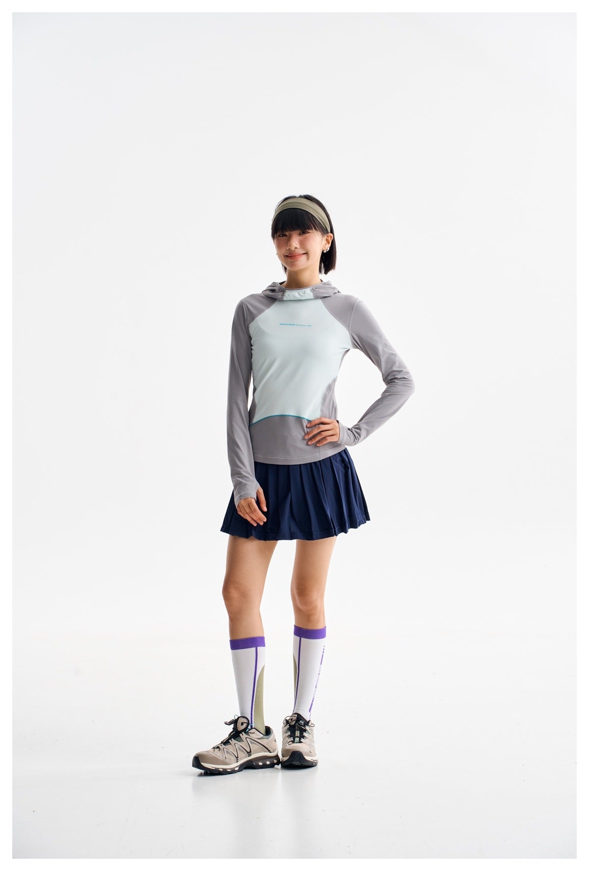 Model wearing a pale mint and gray hooded top, navy pleated skirt, knee-high socks, and sneakers.