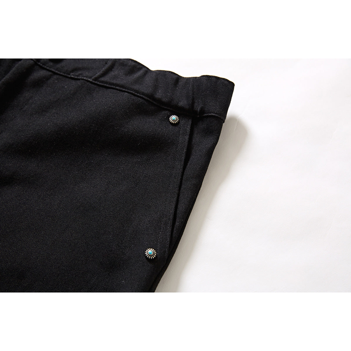 Close-up of black shorts showing a side seam and small decorative turquoise-centered metal studs.