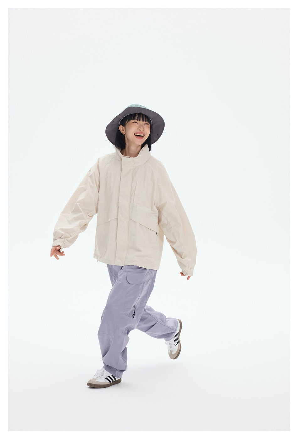 Model in a cream hooded jacket and lavender cargo pants, shown walking in a studio.