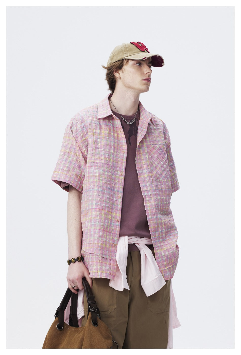 Model in a pastel pink plaid short-sleeve shirt with a chest pocket, shown from cap to upper legs.