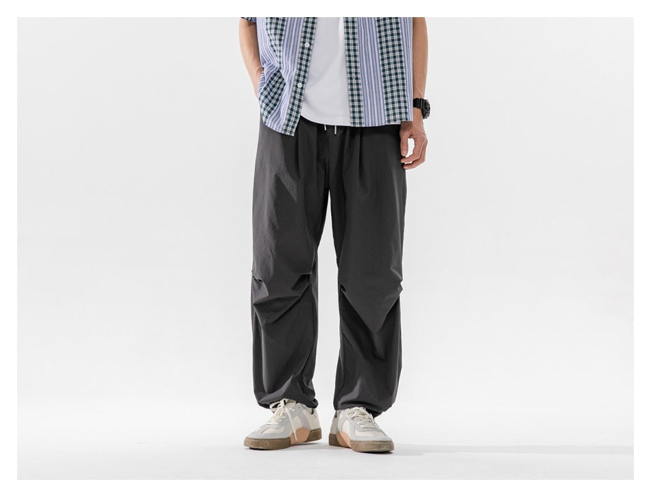 Front view of a cropped model wearing loose charcoal-gray drawstring trousers with a wide leg.