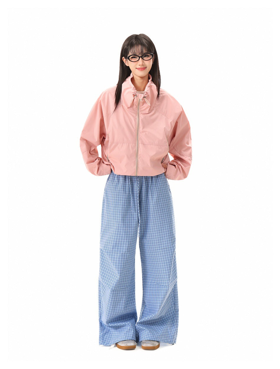 Model wearing a pale pink zip-front jacket with a high gathered collar and wide blue checked trousers, front view.