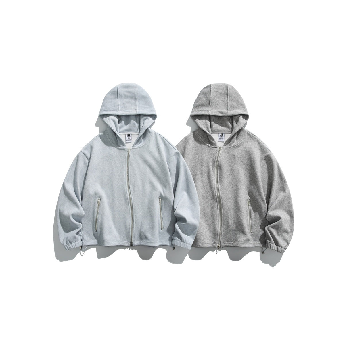 Two hooded zip-up jackets shown from the front in pale gray and heather gray, with zip pockets and gathered cuffs.