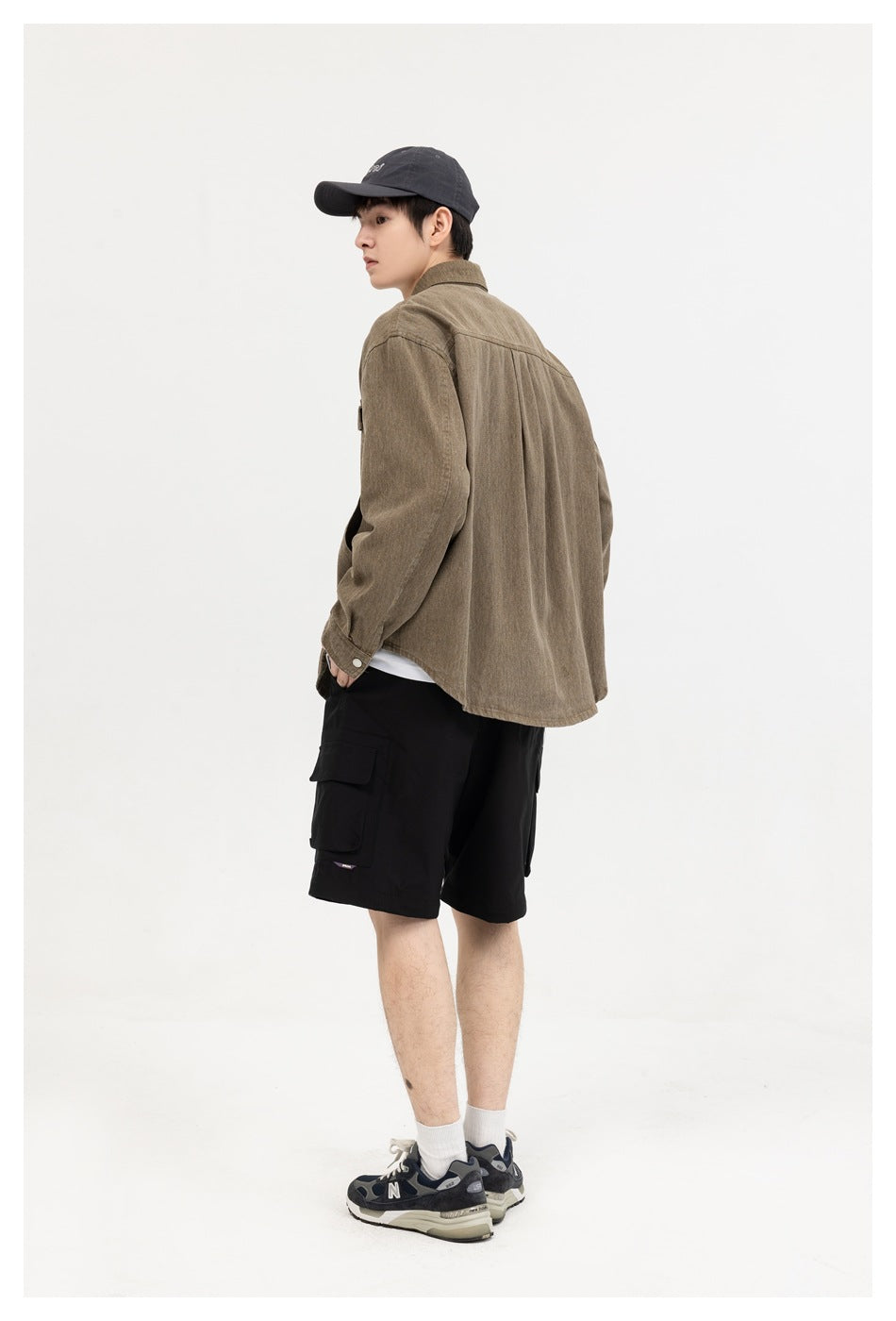 Rear three-quarter view of a model wearing a brown overshirt with a plain back and black cargo shorts.