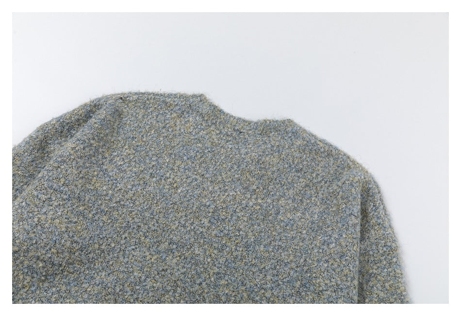 Close-up of the shoulder and upper edge of a mottled gray-blue and beige knit garment against white.