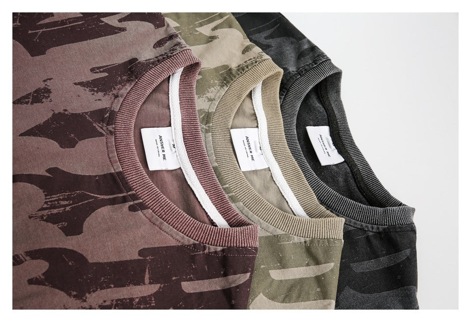 Close-up of three camouflage-print T-shirts in muted mauve, khaki, and black, showing their ribbed crew necks.
