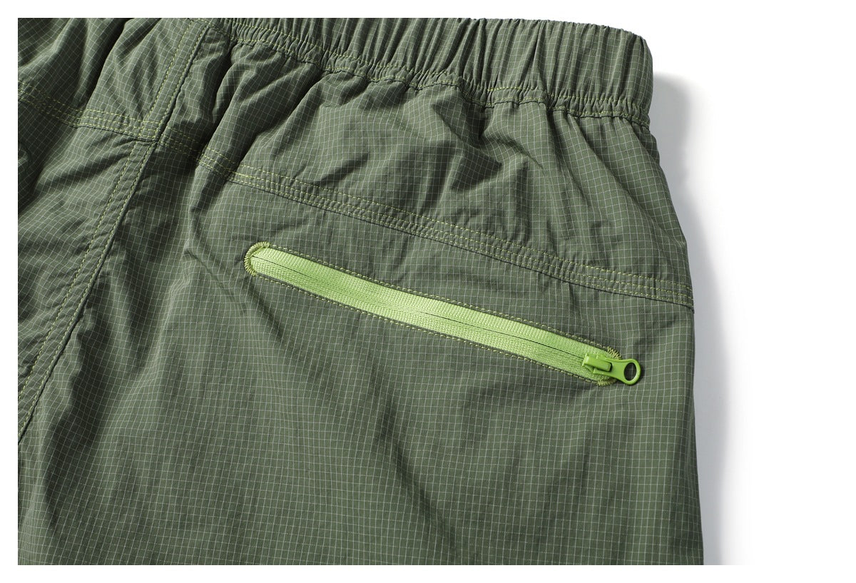 Close-up of olive green grid-patterned garment with an elastic waistband and a diagonal lime-green zip pocket.