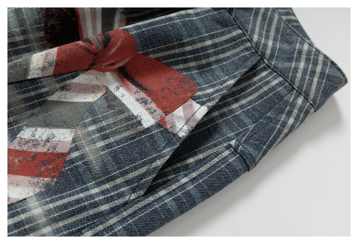 Close-up of plaid trousers showing distressed red, white, and gray printed graphics and a stitched seam.