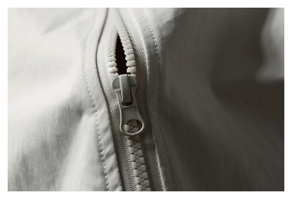 Close-up of a light gray jacket's chunky front zipper and stitched fabric.