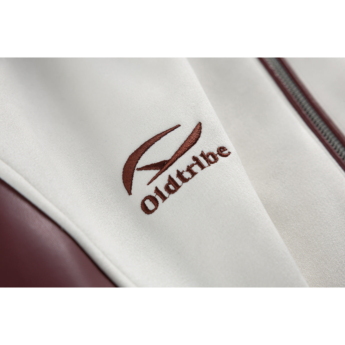 Close-up of burgundy embroidered lettering and emblem on the white fabric of a jacket.