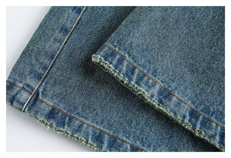 Close-up of blue washed denim showing a frayed, distressed hem with orange topstitching.