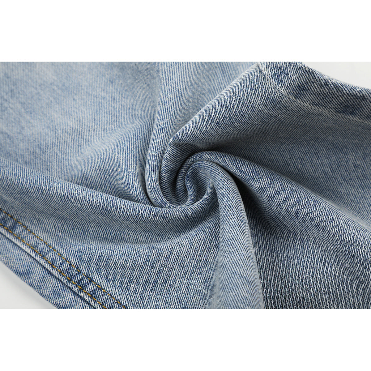 Close-up of light-blue denim gathered into folds, with a line of contrast stitching visible.