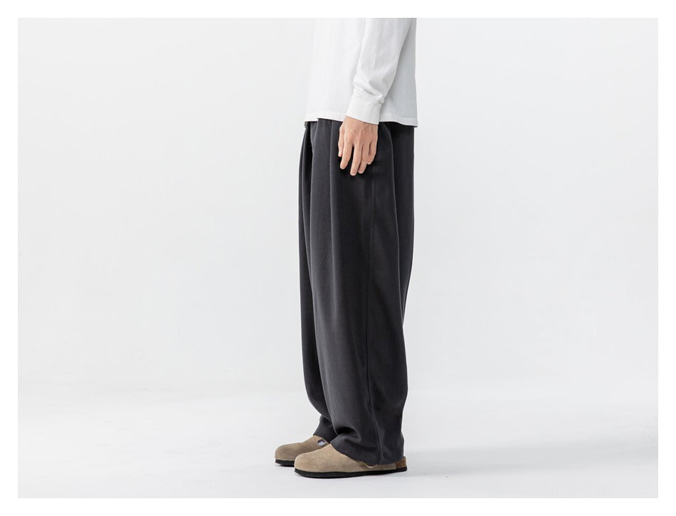 Side view of a person wearing loose charcoal trousers and a white long-sleeve shirt.