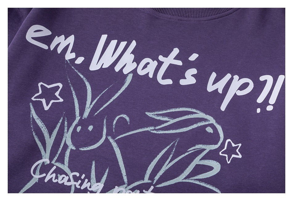 Close-up of a purple sweatshirt chest with white English lettering, stars, and a playful rabbit illustration.