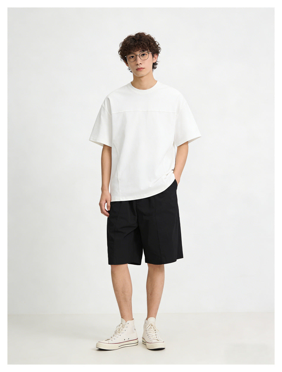 Front view of a model wearing a white oversized short-sleeve T-shirt with a horizontal chest seam and black shorts.