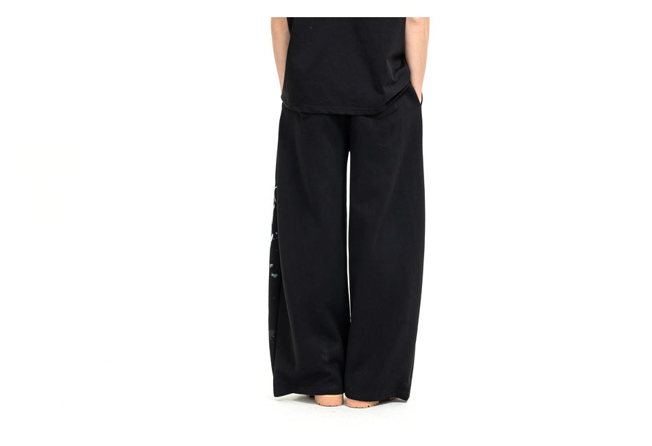 Rear view of black wide-leg pants worn by a model; a small edge of the leg graphic is visible.