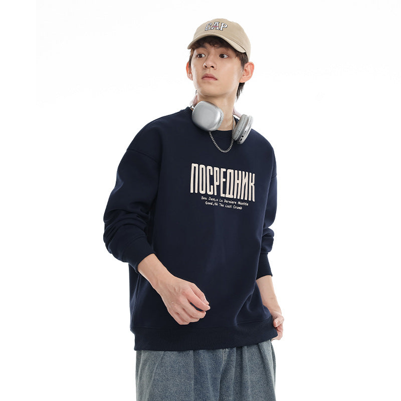 Model wearing a navy crewneck sweatshirt with cream chest lettering and ribbed trim.