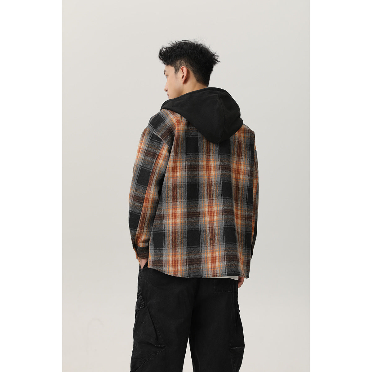 Back view of a man wearing a black, gray, and orange plaid overshirt with a solid black hood.