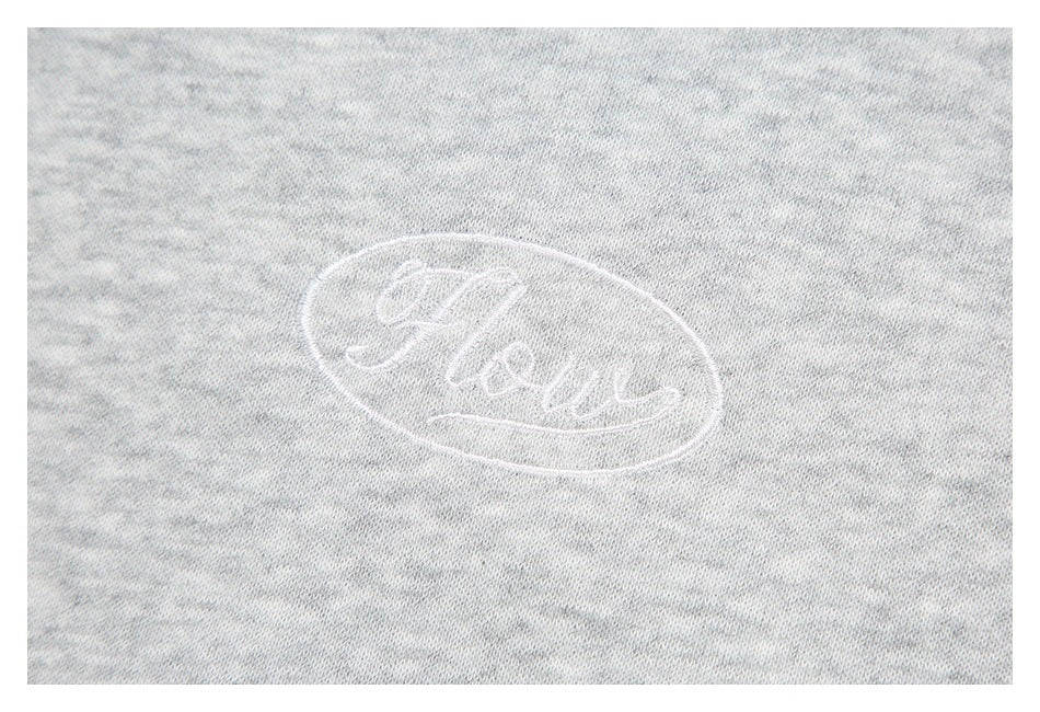 Close-up of a small white oval embroidered script emblem on light heather-gray fabric.