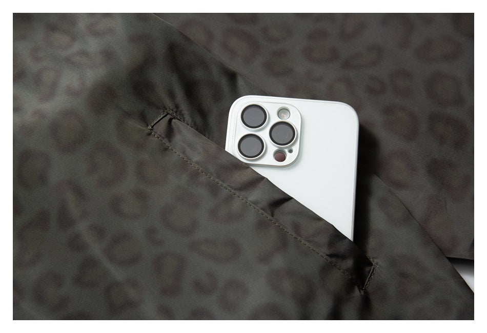 Close-up of a dark gray leopard-print jacket pocket holding a white smartphone.