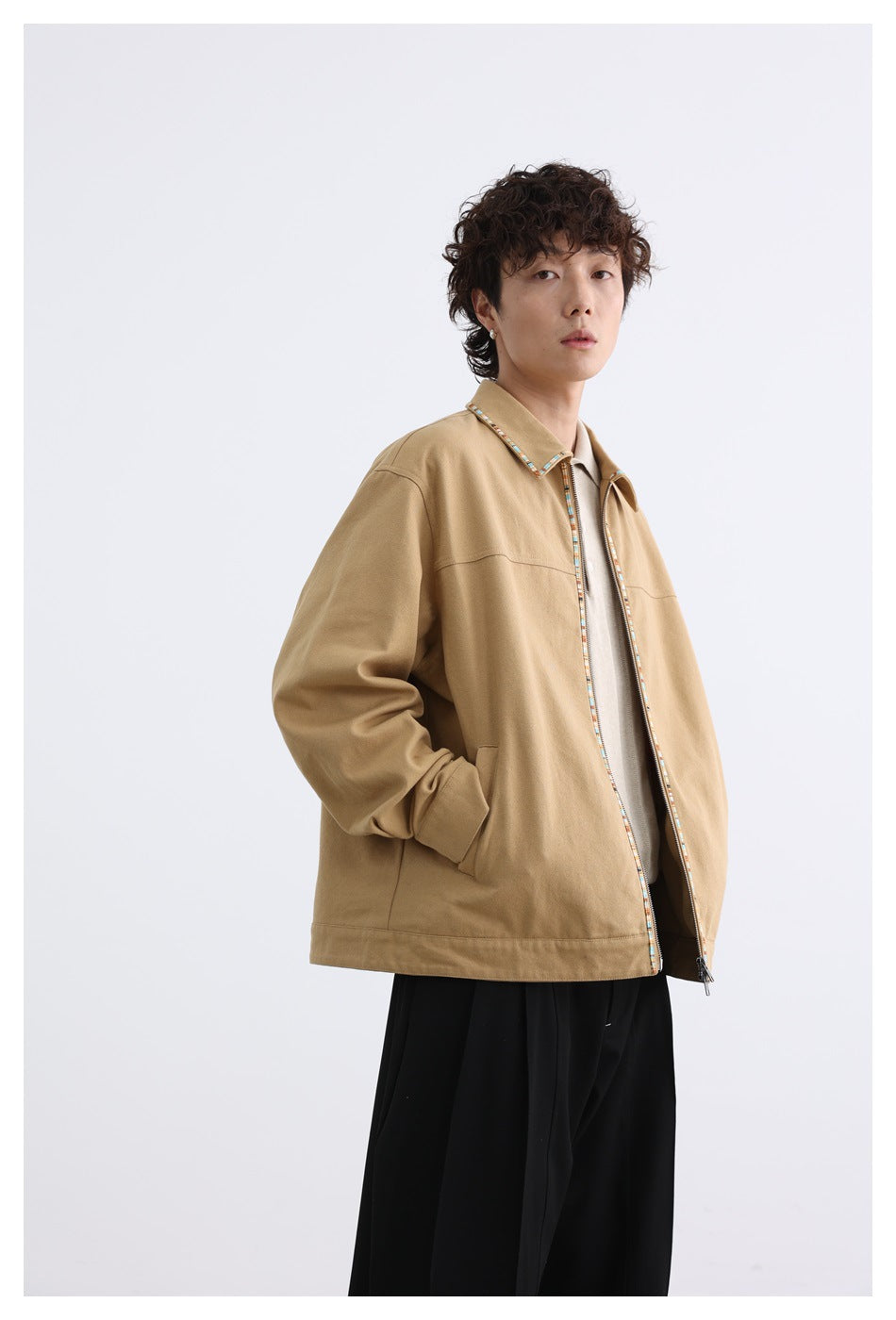 Three-quarter view of a model wearing a tan zip-front jacket with multicolor trim and black trousers.