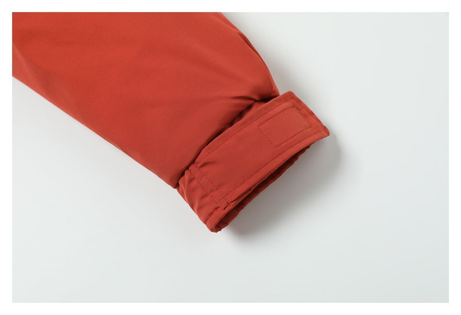 Close-up of a rust-red coat sleeve cuff with a hook-and-loop adjustment tab.