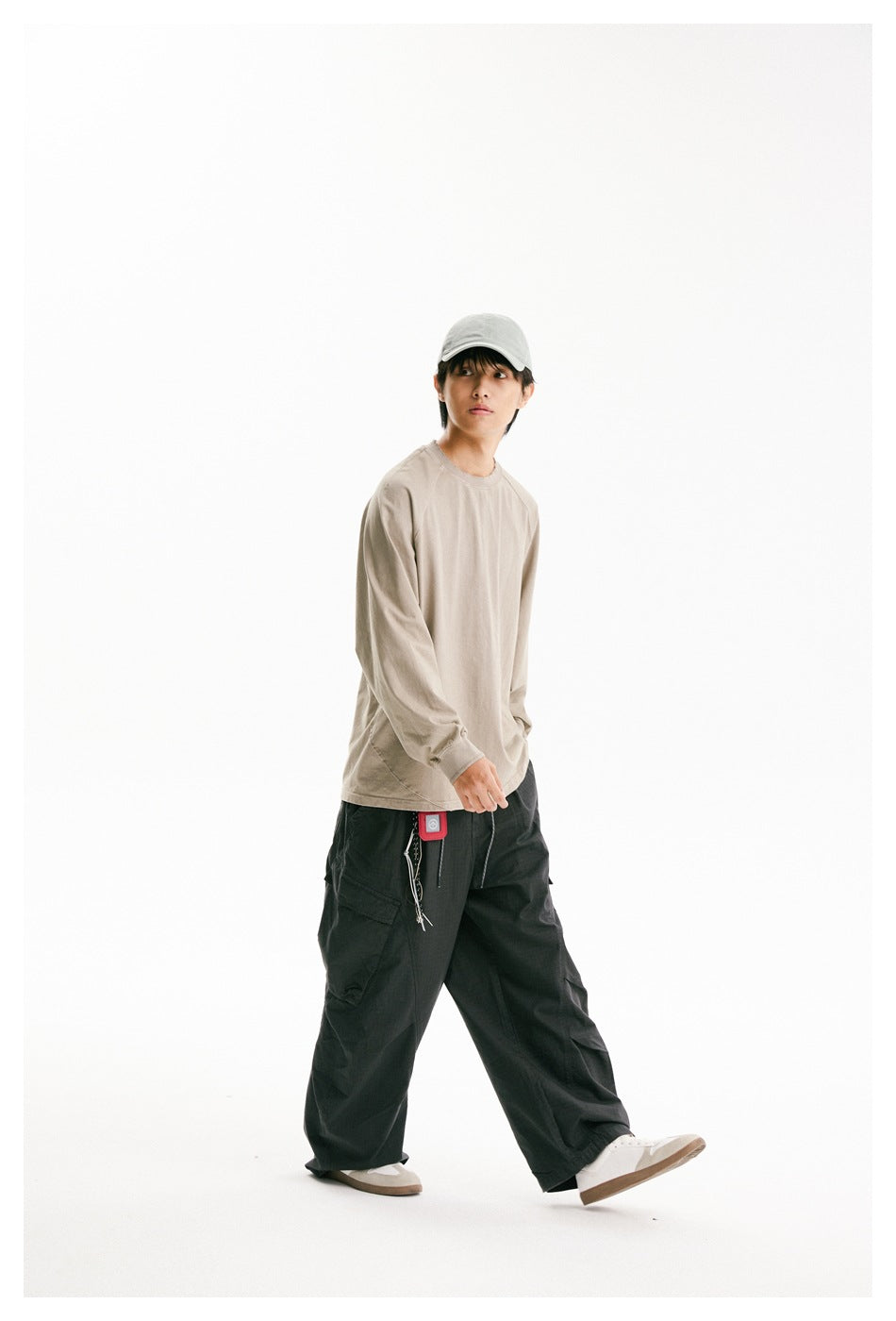 Model walking in a loose beige long-sleeve raglan shirt and dark cargo pants.
