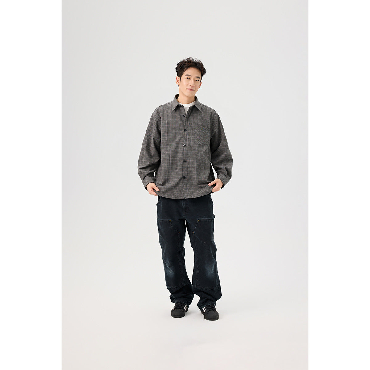 Full-length model wearing a gray plaid button-front overshirt, white tee, loose black pants, and black sneakers.