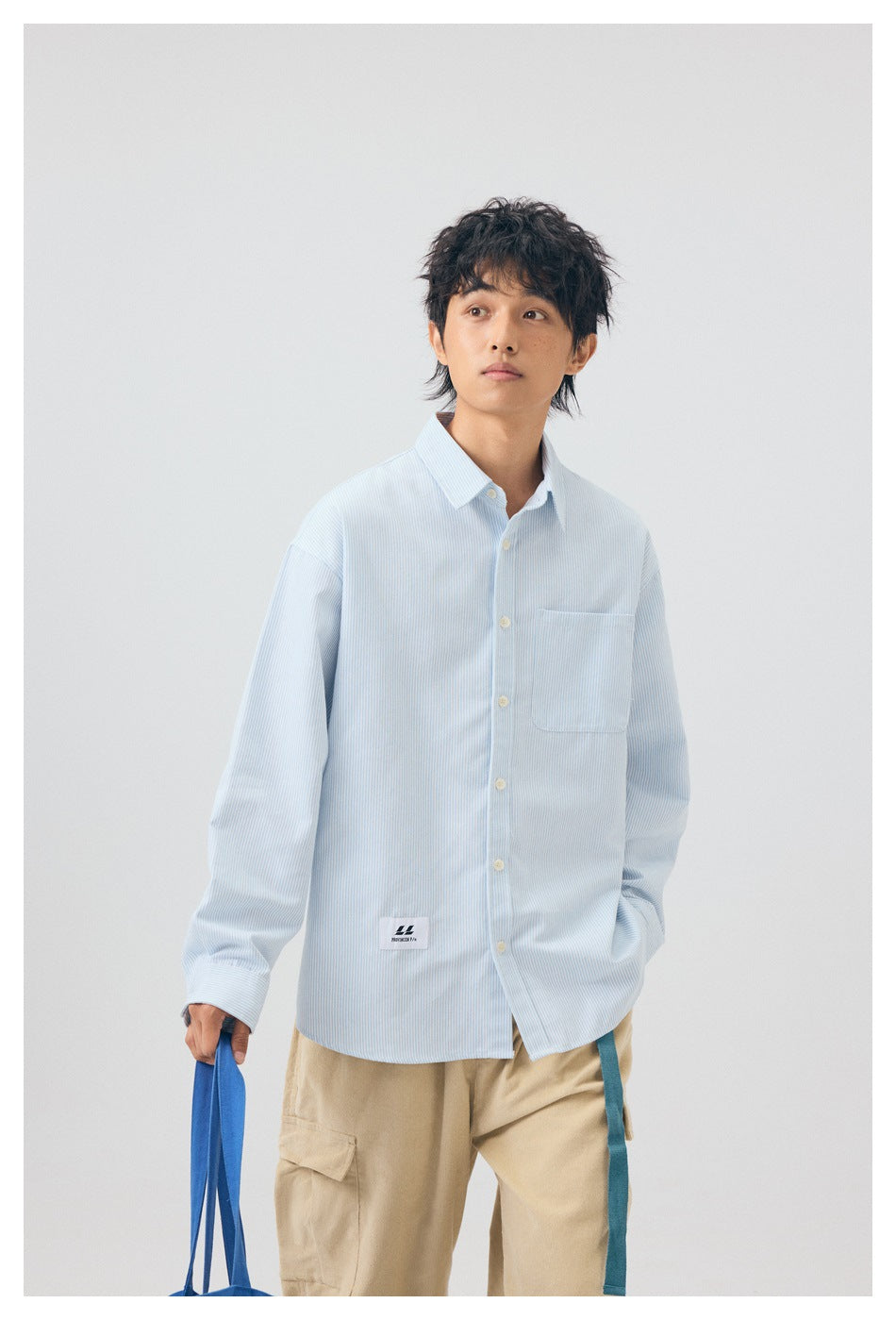 Model wearing a pale blue and white pinstriped button-up shirt with a chest pocket and relaxed fit.