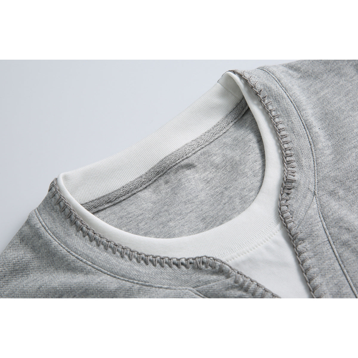 Close-up of a light gray shirt’s stitched neckline layered over a white crew neck.
